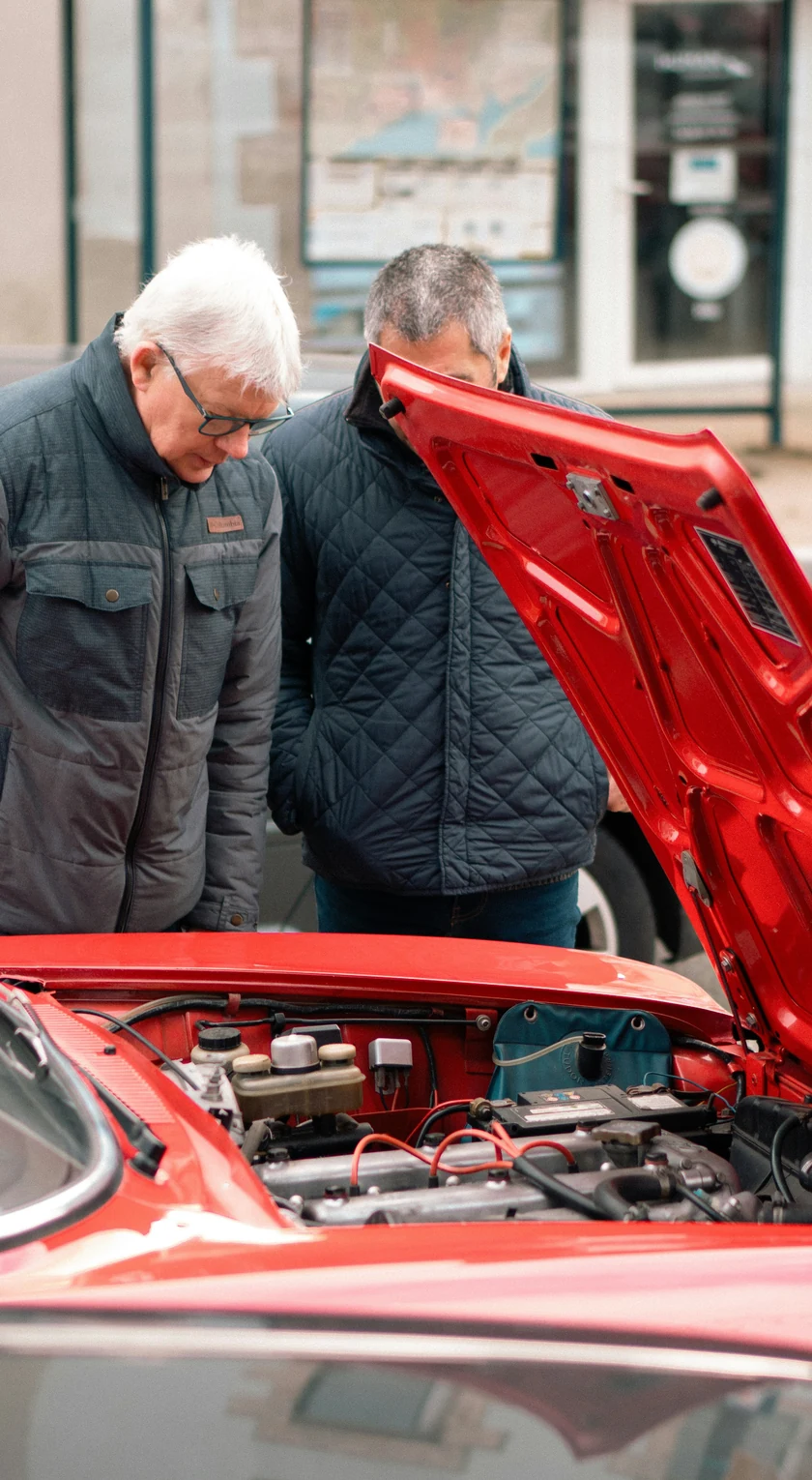 Zwei Männer begutachten den geöffneten Motorraum eines roten Oldtimers