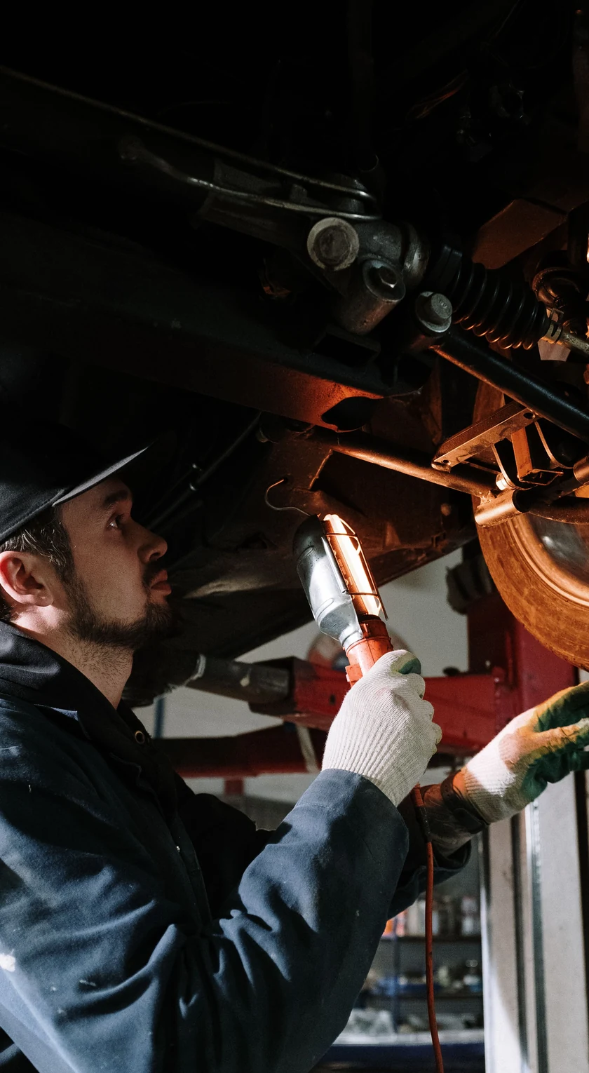 Prüfer untersucht mit einer Inspektionslampe Fahrwerk und Radaufhängung auf der Hebebühne