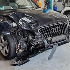 Dunkelblauer Audi Q5 mit zerstörter Front in einer Werkstatt, Motorhaube aufgestaucht, Stoßfänger abgerissen