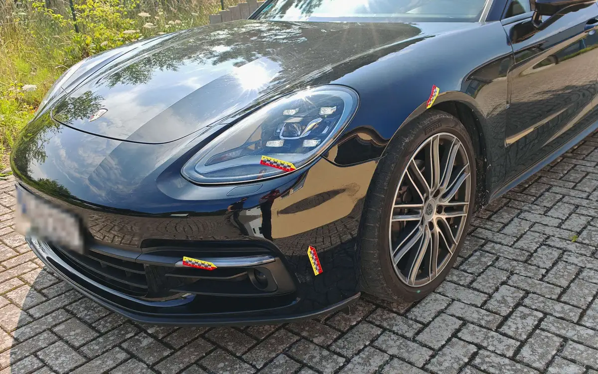 Schwarzer Porsche Panamera mit Frontschaden, Schadenstellen mit Markierungspfeilen gekennzeichnet