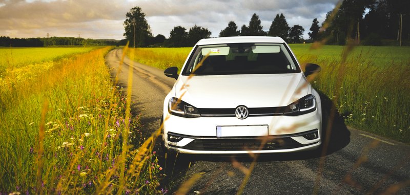 Weißer VW Golf auf einem Feldweg zwischen Wiesen