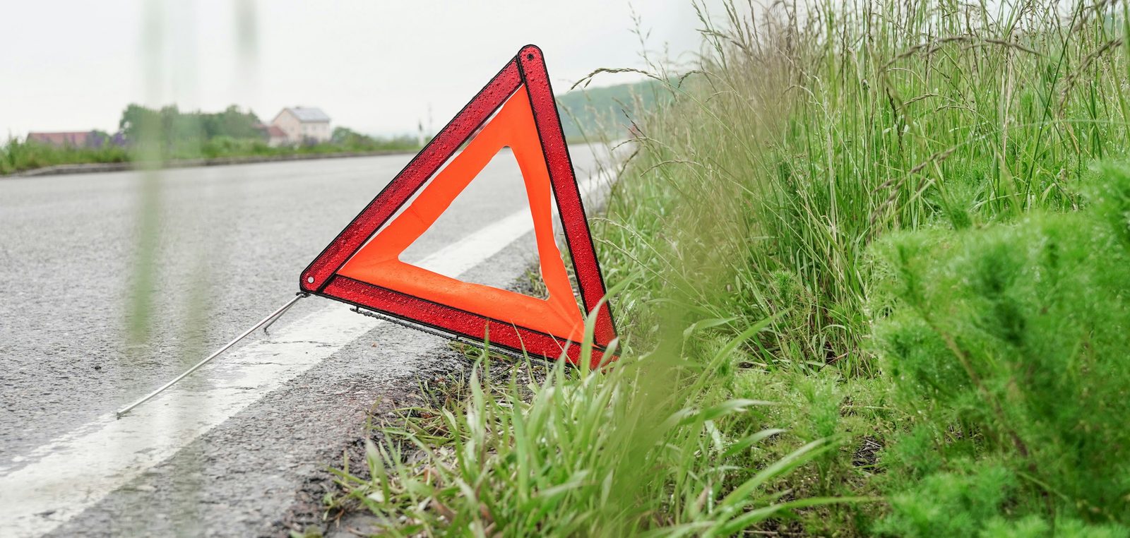 Rotes Warndreieck steht am Rand einer nassen Landstraße