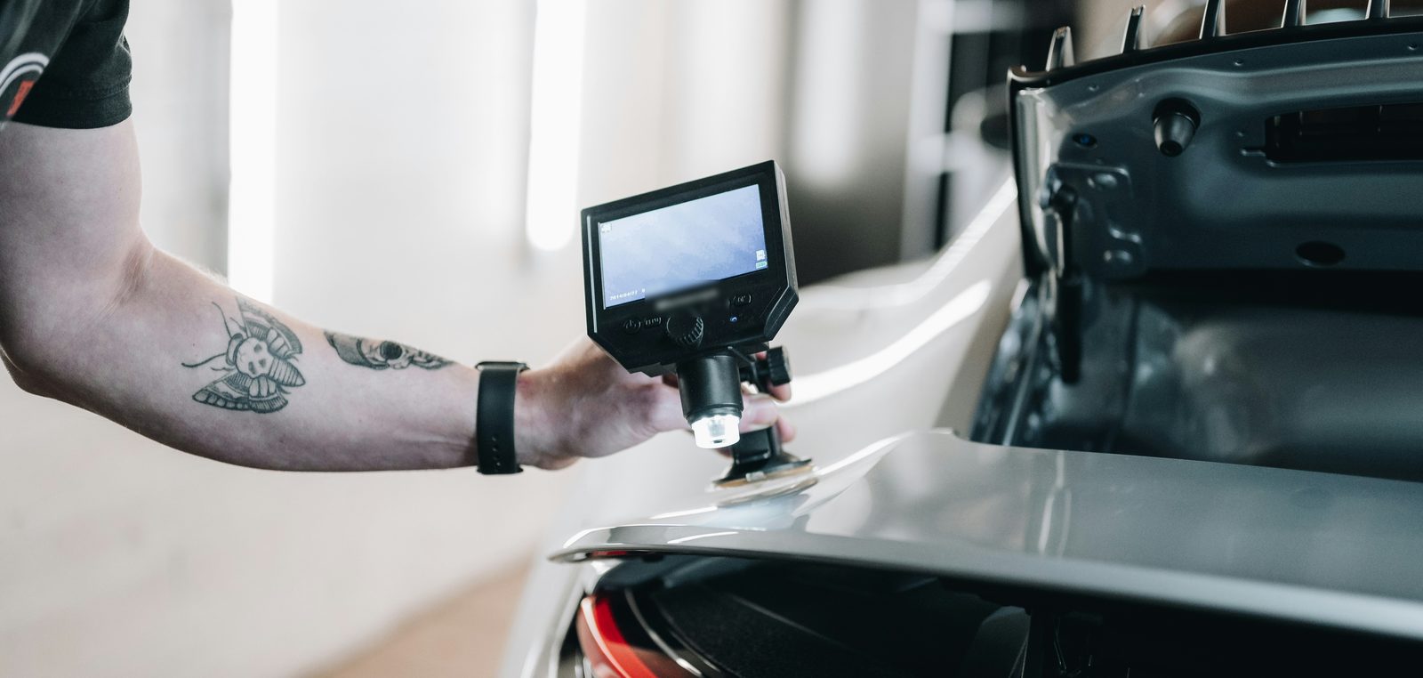 Hand setzt ein digitales Messmikroskop auf den Lack eines Autos