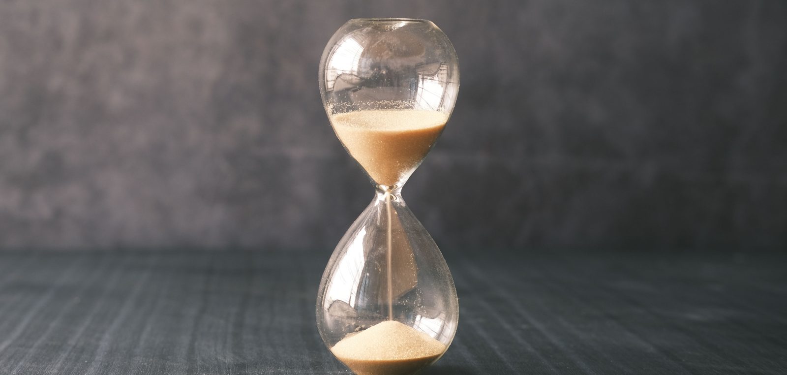 Sanduhr mit hellem Sand vor grauer Wand