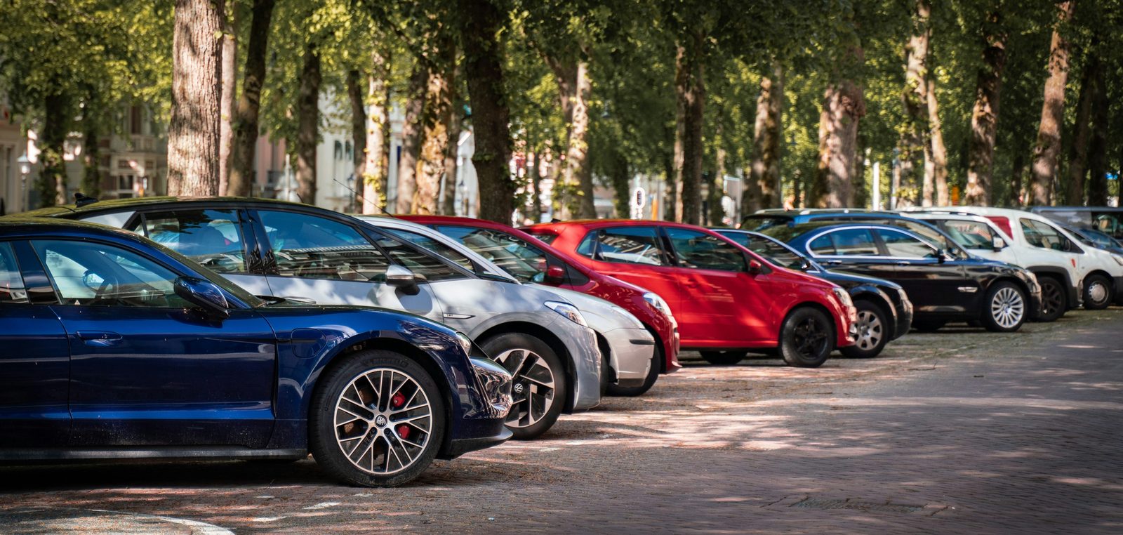 Reihe geparkter Autos unter Bäumen auf einem Parkplatz