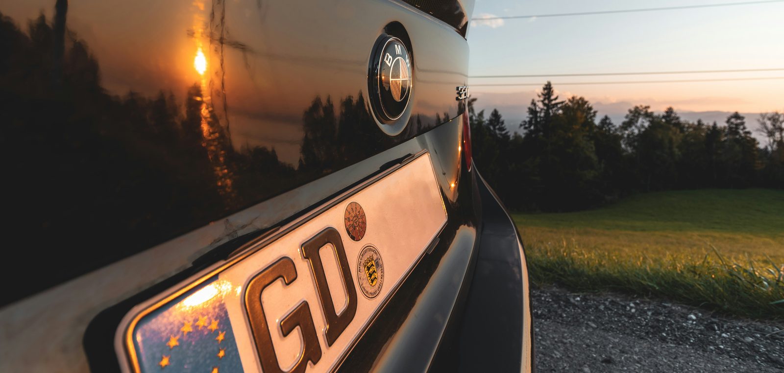 Deutsches Kennzeichen mit HU-Prüfplakette am Heck eines dunklen Autos im Abendlicht