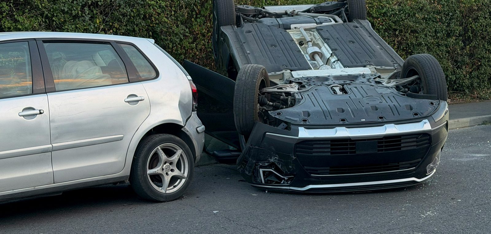 Überschlagenes Auto neben einem beschädigten silbernen Kleinwagen nach einem Unfall