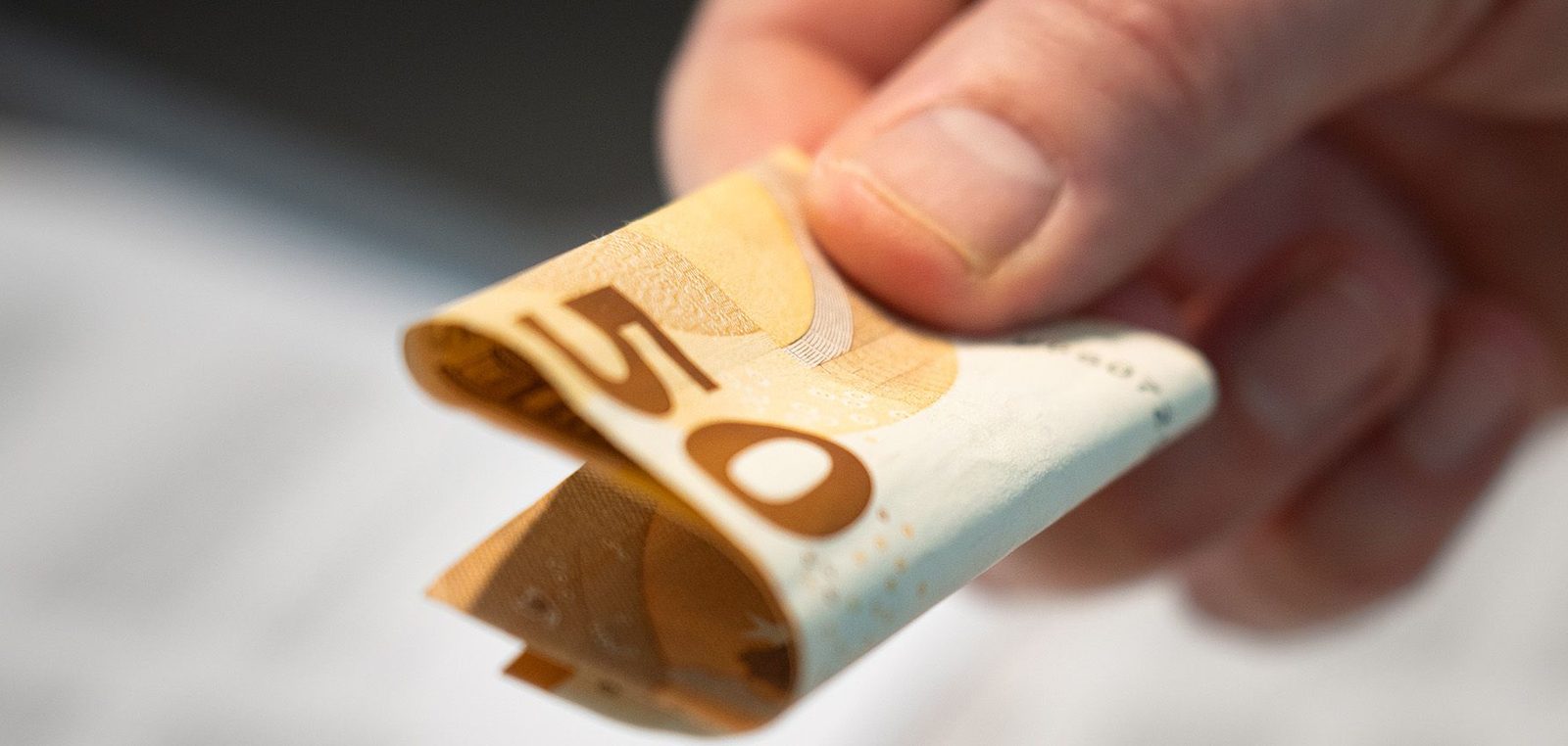 Hand reicht einen 50-Euro-Schein über Rechnungsunterlagen und einen Taschenrechner