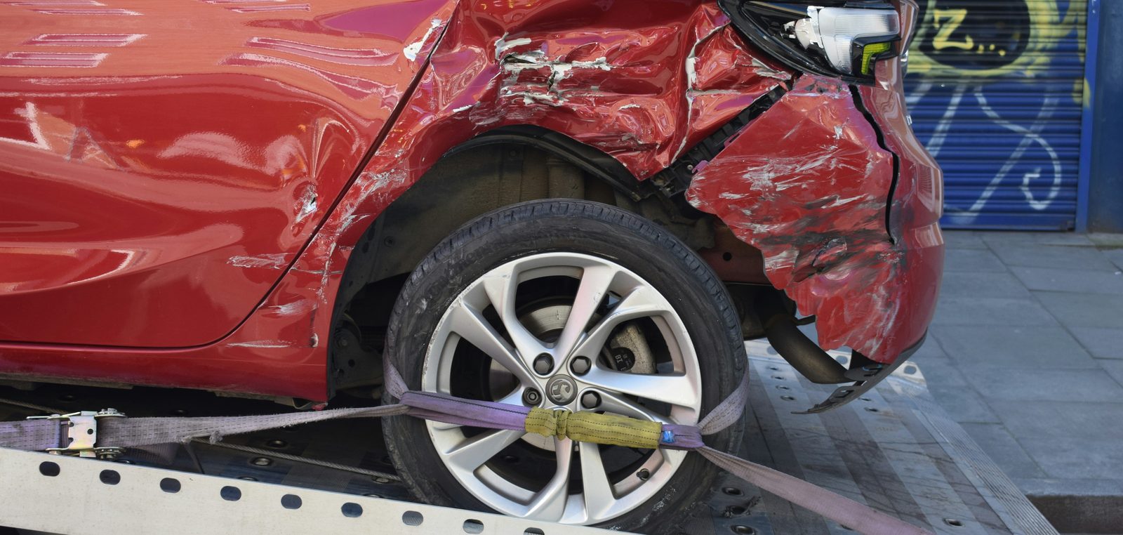 Beschädigtes rotes Auto ist mit Spanngurten auf der Ladefläche eines Abschleppwagens gesichert