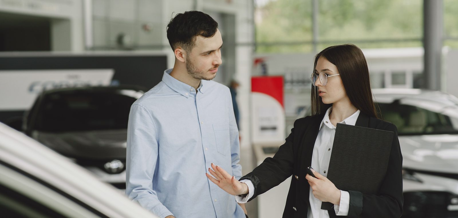 Verkäuferin im Autohaus wehrt mit erhobener Hand das Anliegen eines Kunden ab